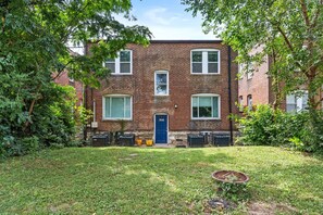 A two-story brick building with a blue door, surrounded by a grassy yard and trees. - The Cove | A St. Louis Retreat by StayLage (Saint Louis)