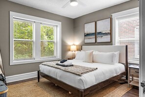 A bedroom with a bed, two bedside lamps, a window with blinds, and a ceiling fan. - The Cove | A St. Louis Retreat by StayLage (Saint Louis)