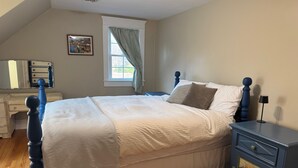 Un dormitorio con cama, mesita de noche, cómoda, ventana con cortinas y un cuadro en la pared.