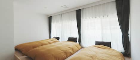 A bedroom with two beds, a window with sheer curtains, and a wooden floor.
