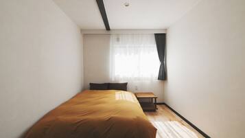 Un dormitorio con una cama, una mesita y una ventana con cortinas.
