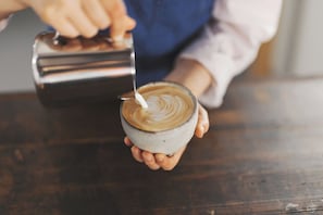 A person holding a cup of coffee with latte art, using a metal pitcher to pour. - kadoya (Kosuge)