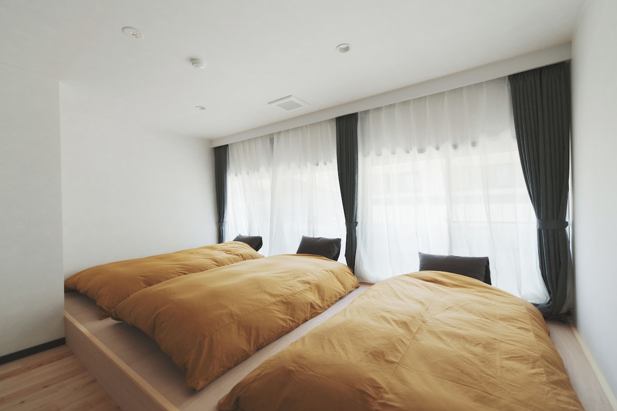 Une chambre avec deux lits, une fenêtre avec des rideaux légers et un plancher en bois.
