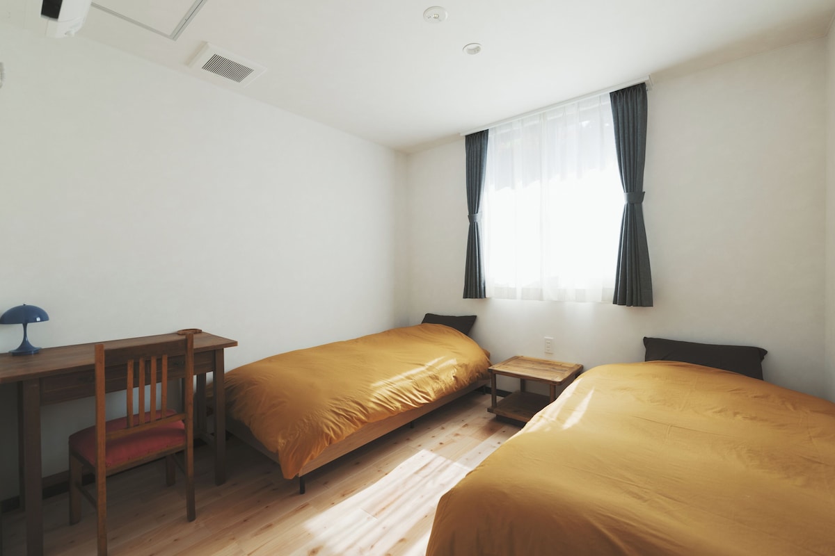 Une chambre avec deux lits simples, un bureau, une chaise et une petite table.
