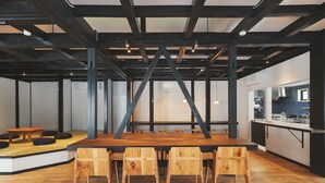 A spacious room with a large wooden table and chairs, a kitchen area with blue tiles, and exposed wooden beams on the ceiling. - kadoya (Kosuge)