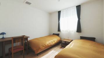 A room with two single beds, a desk, a chair, and a small table.