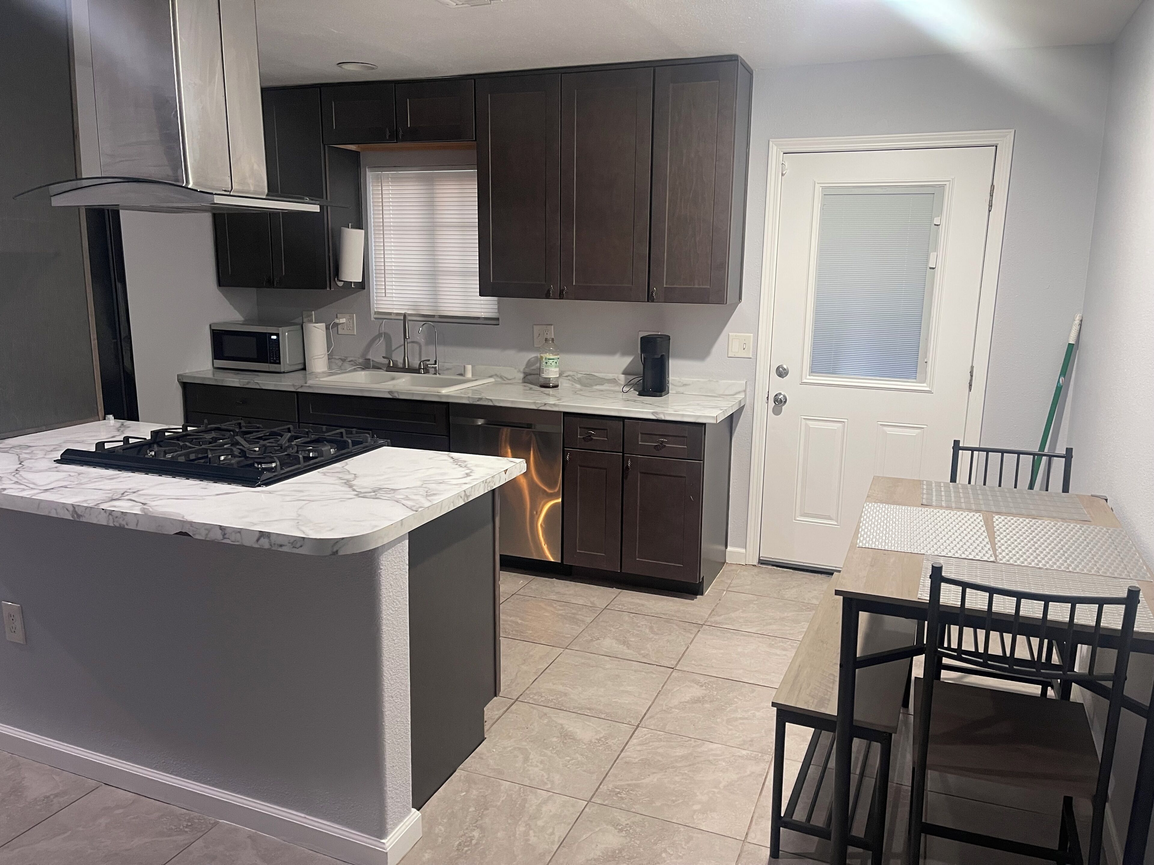 A modern kitchen with dark cabinetry, a central island with a stove, a microwave, and a sink.
