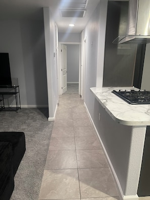 A narrow hallway with a kitchen area on one side, featuring a marble countertop and a gas stove. - The High Desert Hideout - Enjoyable 2-bedroom, 1 bath
Spacious yard, RV parking. (Hesperia)