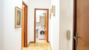 Un couloir avec une machine à laver au fond, une porte sur la droite et un téléphone accroché au mur.