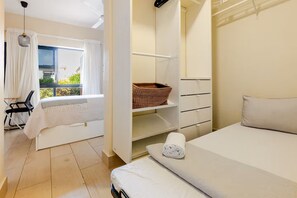 A bedroom with a bed, a window with curtains, a chair, a shelf with a basket, and a bedside table with a rolled towel. - Vista Cana private Jacuzzi + Golf + Beach + Pool (Punta Cana)