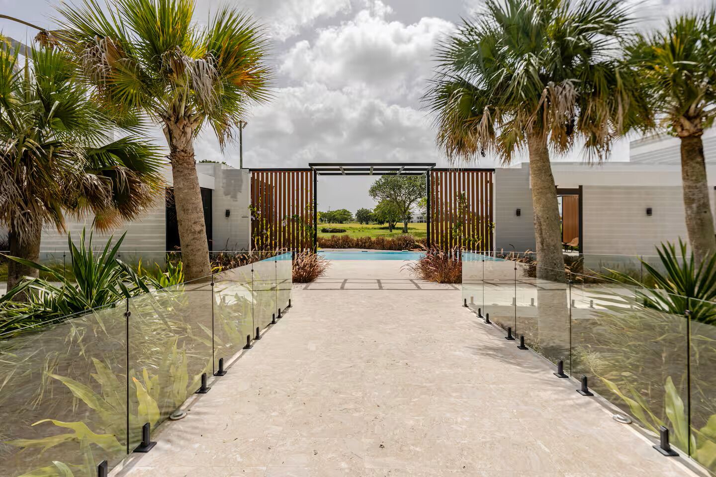 A pathway leading to a pool with palm trees and a modern building in the background.