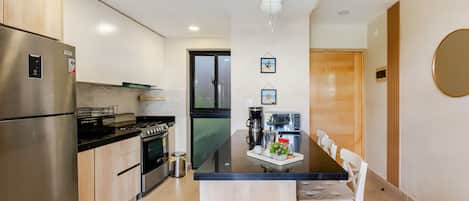 Una cocina moderna con electrodomésticos de acero inoxidable, un comedor con una mesa negra y sillas blancas.
