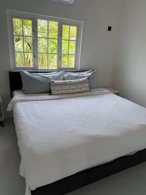 Ein Bett mit weißer, strukturierter Bettdecke, zwei Kissen und ein Fenster mit Blick ins Grüne.
