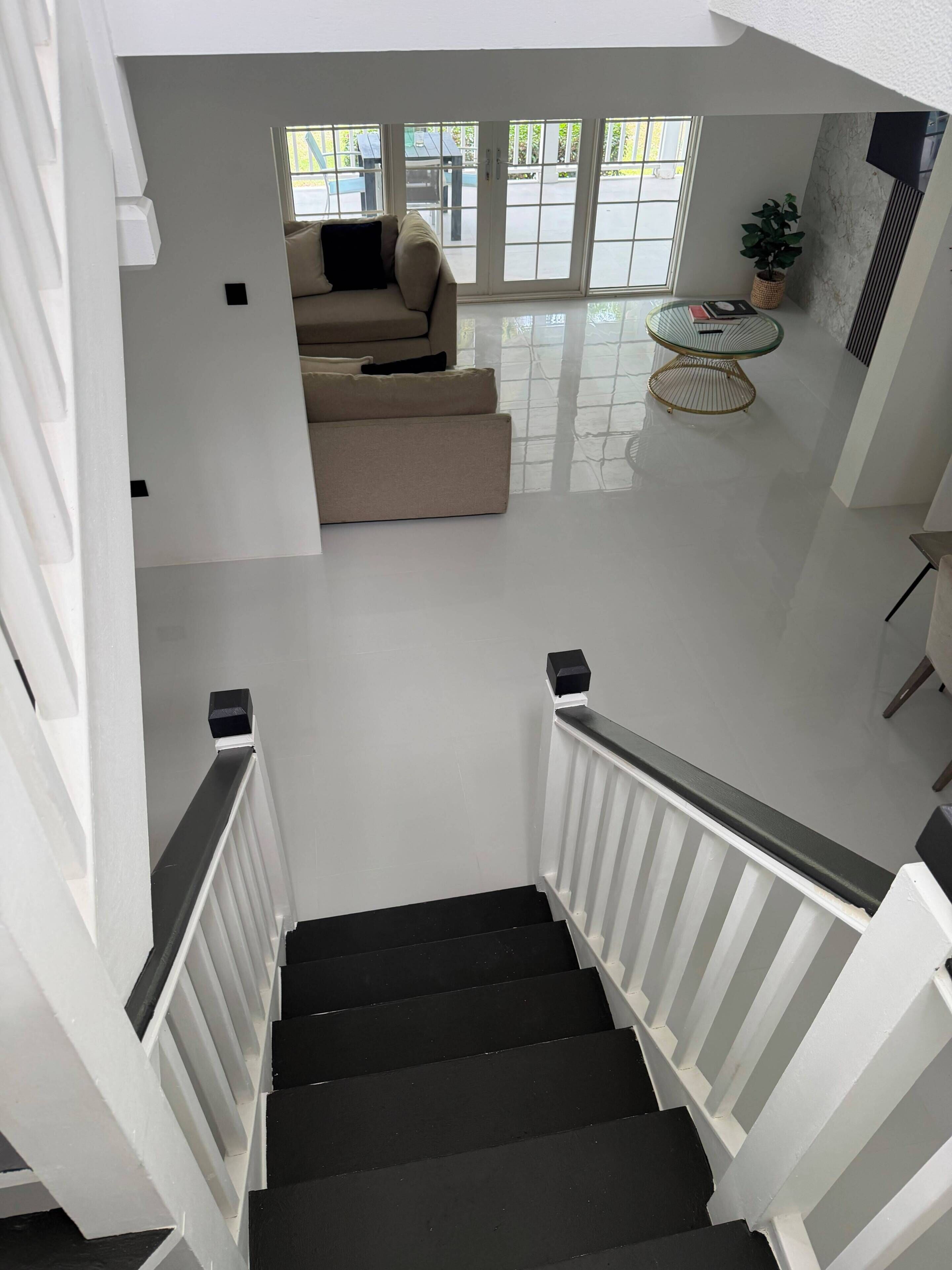 A staircase with white railings and black steps leading to a living area with a sofa and a glass coffee table.