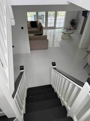 Eine Treppe mit weißen Geländern und schwarzen Stufen führt zu einem Wohnbereich mit einer Couch und einem Glastisch.