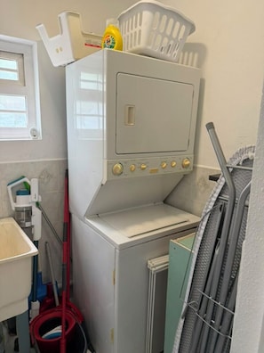 Ein kleiner Waschraum mit einer Waschmaschine, einem Wäscheständer und einem Mopp.