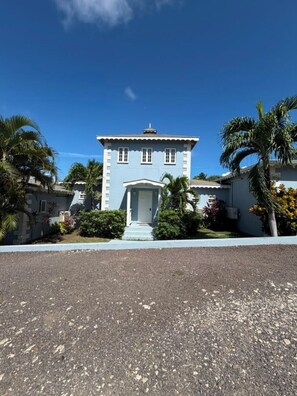 A two-story building with a central entrance, surrounded by palm trees and a clear sky. - Cap Estate 3BR Townhome, Private Plunge Pool, Golf (Gros Islet)