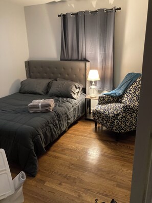 A bedroom with a bed, a nightstand, a lamp, a chair, and a curtain. - 3-bedroom house in terrific Gastonia with cool AC breeze. (Gastonia)