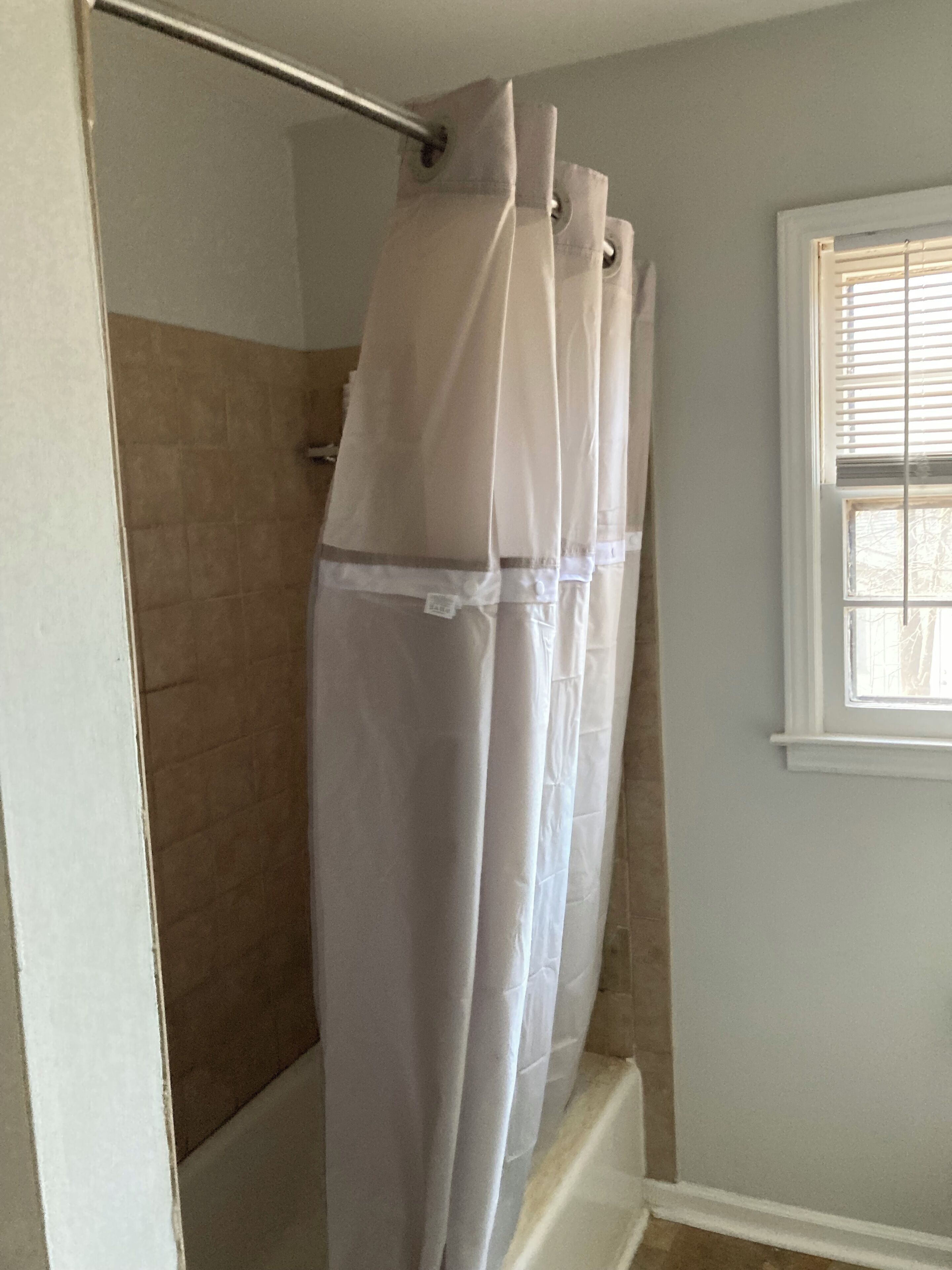 Ein Badezimmer mit Duschvorhang, Fenster mit Jalousien und Fliesenwand.