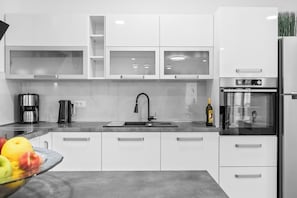 Eine moderne Küche mit weißen Schränken, einem Edelstahlkühlschrank, einer Kaffeemaschine und einer Obstschale.