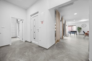 Eine geräumige, moderne Hotelhalle mit grau gefliestem Boden, einem Essbereich mit Tisch und Stühlen sowie einer Wanduhr.