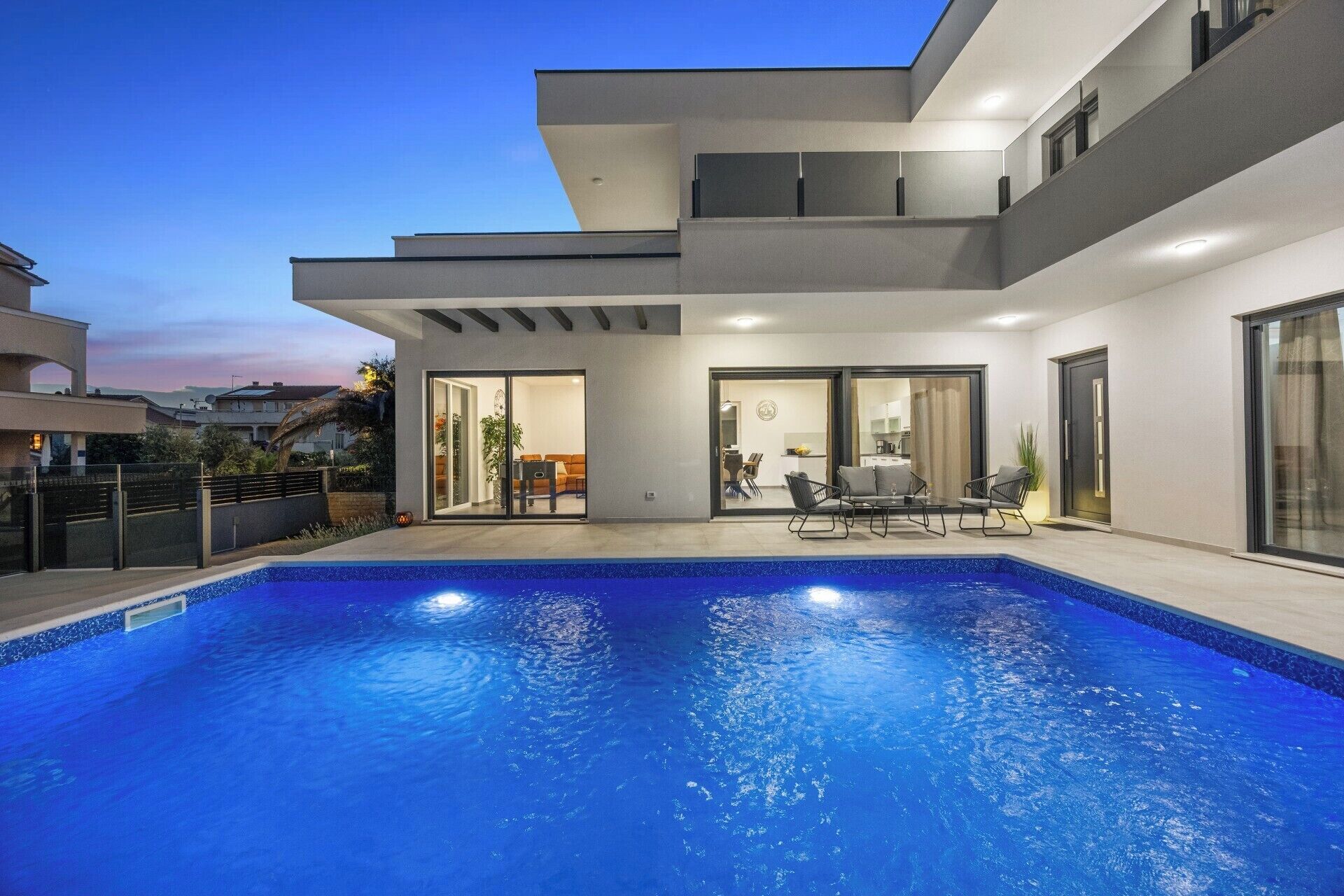 A modern house with a swimming pool, a dining area, and a kitchen visible through glass doors.