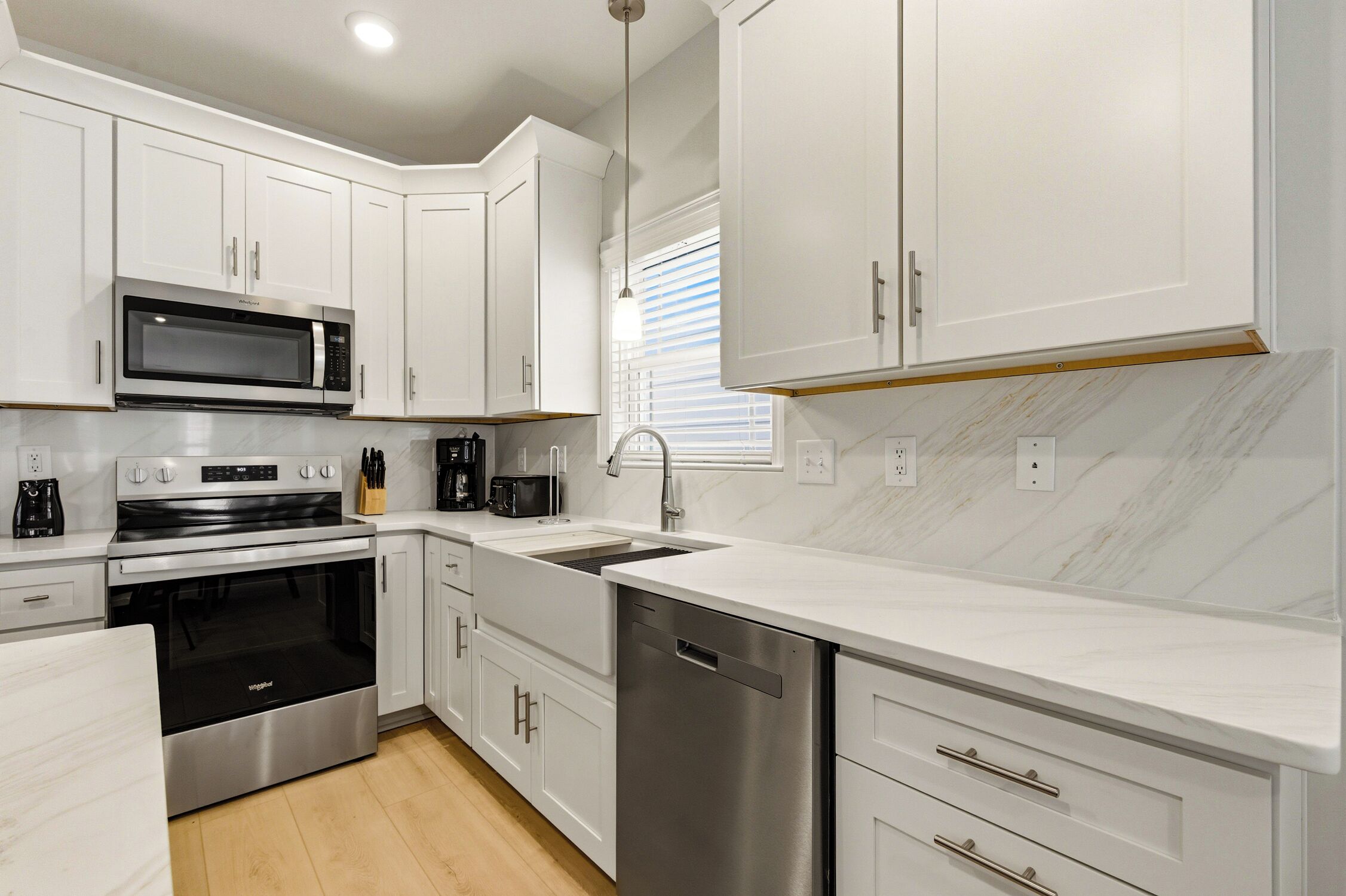 A modern kitchen with white cabinetry, stainless steel appliances, and a marble backsplash.