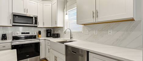 A modern kitchen with white cabinetry, stainless steel appliances, and a marble backsplash.