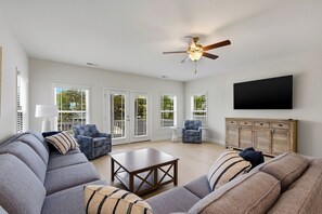 A spacious living room with a grey sectional sofa, a coffee table, and a ceiling fan. - Walkin' On Sunshine - Walk to Surfside Beach! (Surfside Beach)
