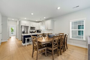 A modern kitchen with white cabinets, stainless steel appliances, and a central island with bar stools. - Walkin' On Sunshine - Walk to Surfside Beach! (Surfside Beach)