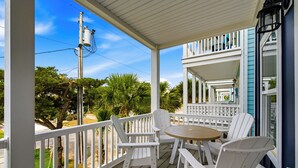 A covered porch with white railings, a round wooden table, and white chairs.