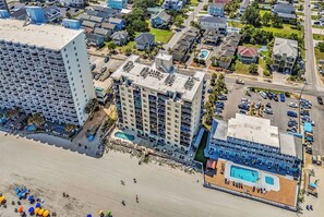 Un hotel frente al mar con varias construcciones, zona de playa y piscina.