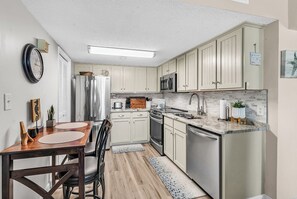 Cocina compacta con armarios blancos, electrodomésticos de acero inoxidable y una mesa de comedor de madera.
