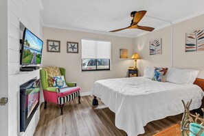Quarto com cama, uma cadeira, televisão e obras de arte nas paredes.