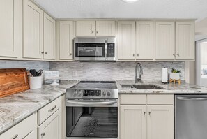 A kitchen with white cabinets, a stainless steel microwave, a stove, and a dishwasher. - Horizon East Cabana 4 - Oceanfront in Garden City Beach (Garden City Beach)