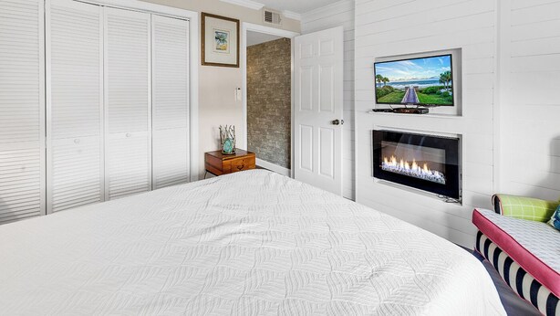 Ein Schlafzimmer mit einem großen Bett, einem an der Wand montierten Fernseher, einem Kamin und einem Kleiderschrank mit Schiebetüren.