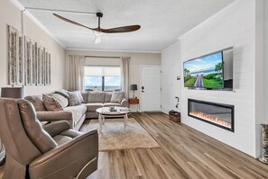 Una sala de estar moderna con sofá, sillones, una mesa de centro, chimenea, televisor y ventilador de techo.