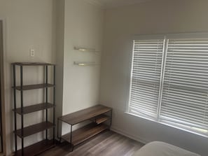 A room with a wooden floor, a metal shelving unit, a bench, and a window with blinds. - Gorgeous Executive Master Suite + Private Bedroom 2-bedroom in friendly Mableton (Mableton)