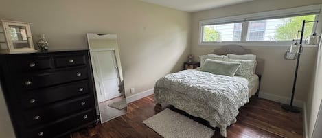 Une chambre à coucher comprenant un lit, une commode, un ventilateur de plafond, une fenêtre et une lampe sur pied.