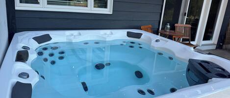 A hot tub with a clear view of the surrounding area, including a house with a pergola and a patio chair.
