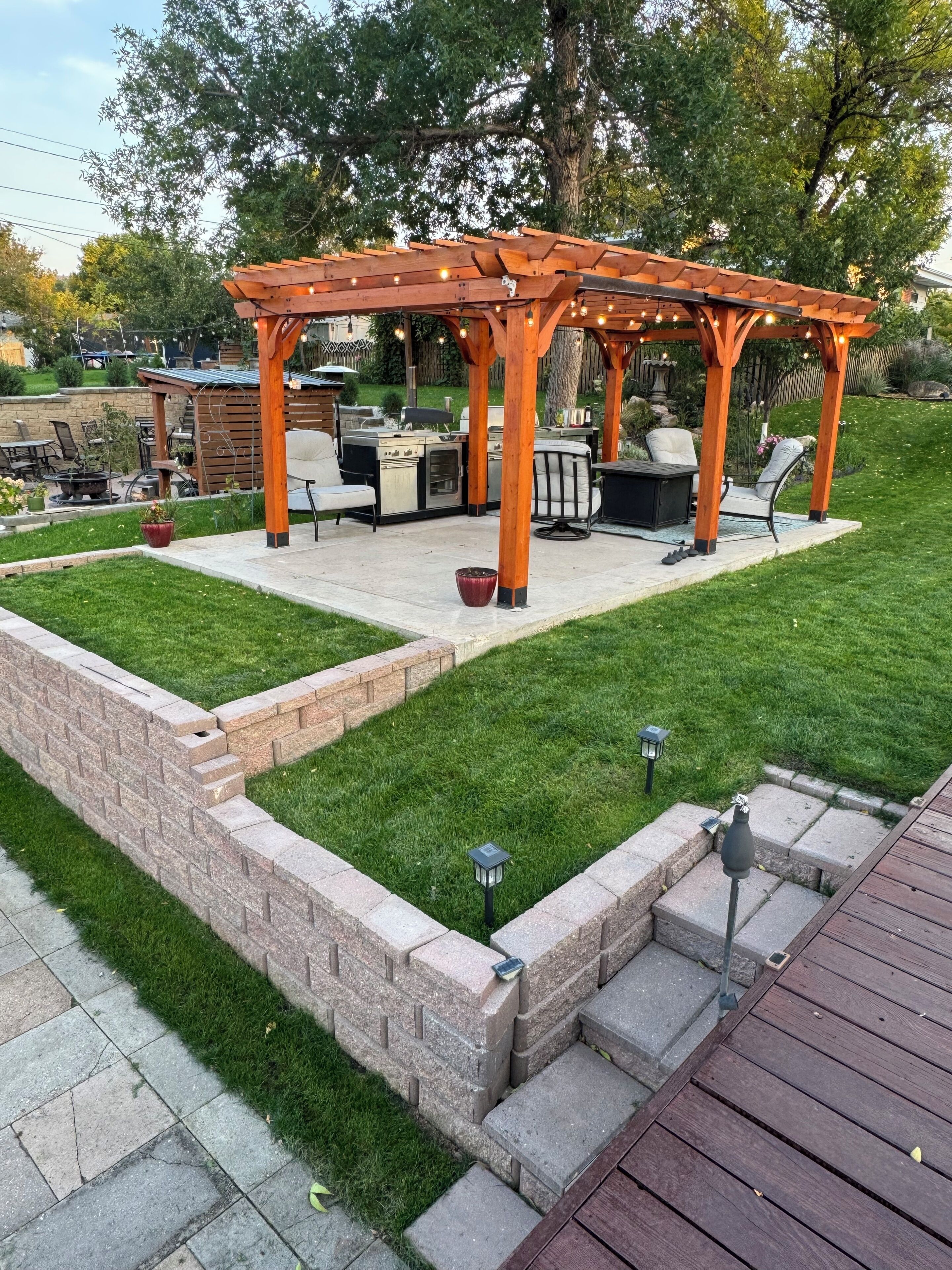 A wooden pergola with a barbecue area, outdoor seating, and a well-maintained lawn.