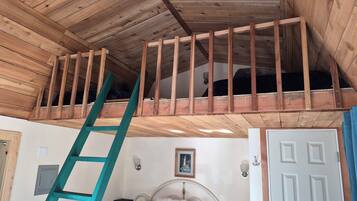A room with a loft bed, a wooden ladder, a white door, and a framed picture on the wall.