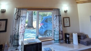 Una habitación con ventilador de techo, ventana con cortinas, microondas, cafetera y un cuadro en la pared.