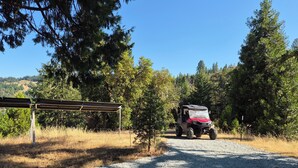 Un camino de grava que conduce a un vehículo rojo estacionado bajo un refugio metálico.