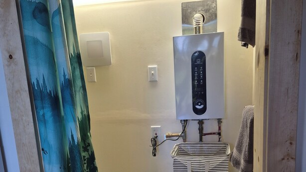 Un baño con cortina de ducha, un perchero, un calentador de agua y una toalla a rayas.