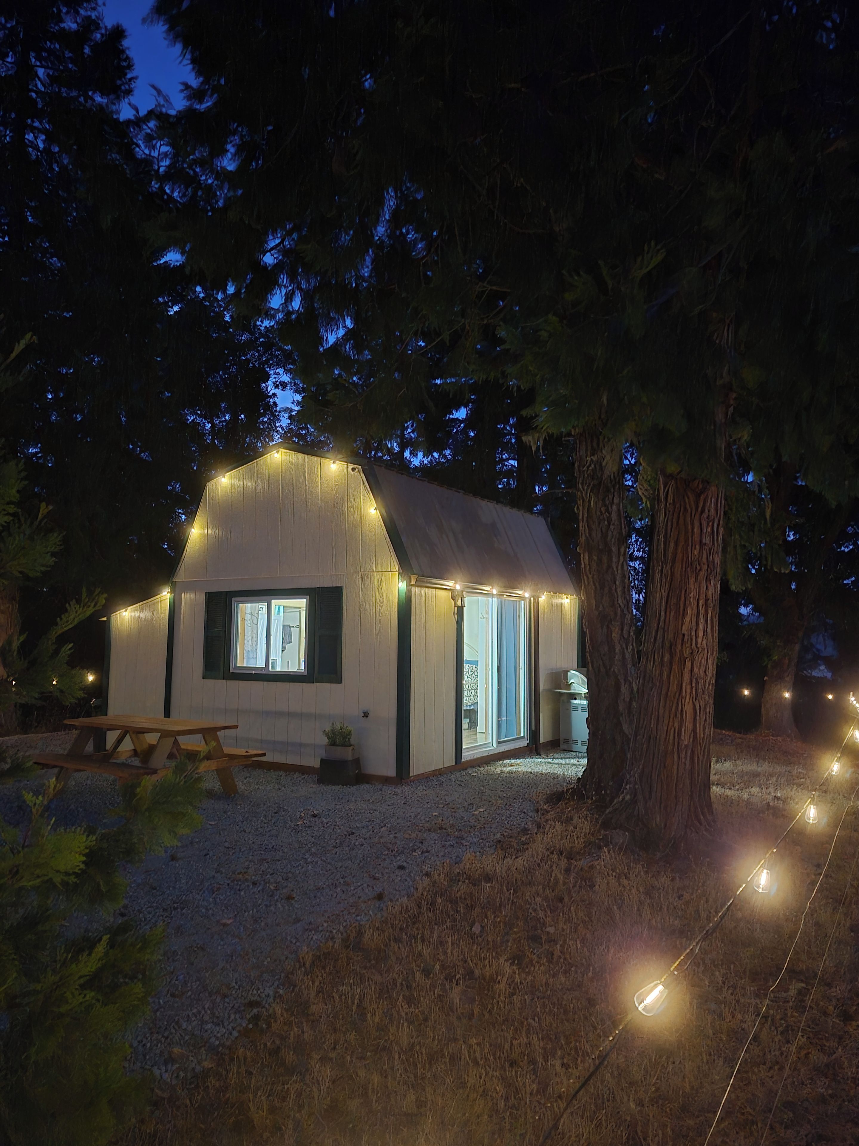 Eine kleine Holzhütte mit geneigtem Dach, einem Holztisch und einer Lichterkette.
