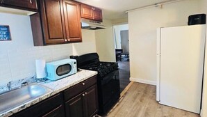 Una cucina compatta con pensili in legno scuro, un frigorifero bianco e un forno a microonde sul piano di lavoro.