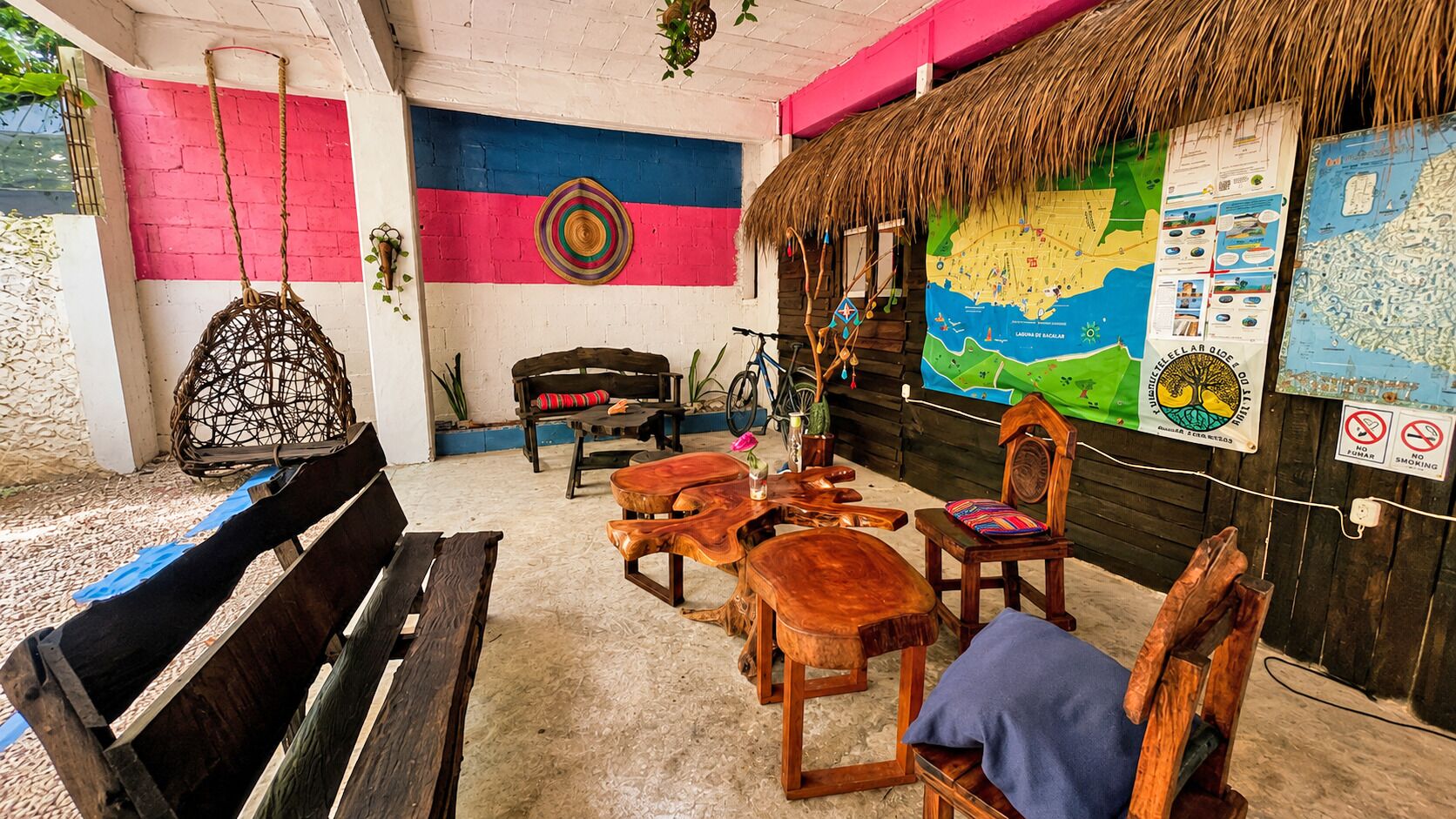 A rustic outdoor seating area with wooden furniture, a hanging chair, and a thatched roof structure.