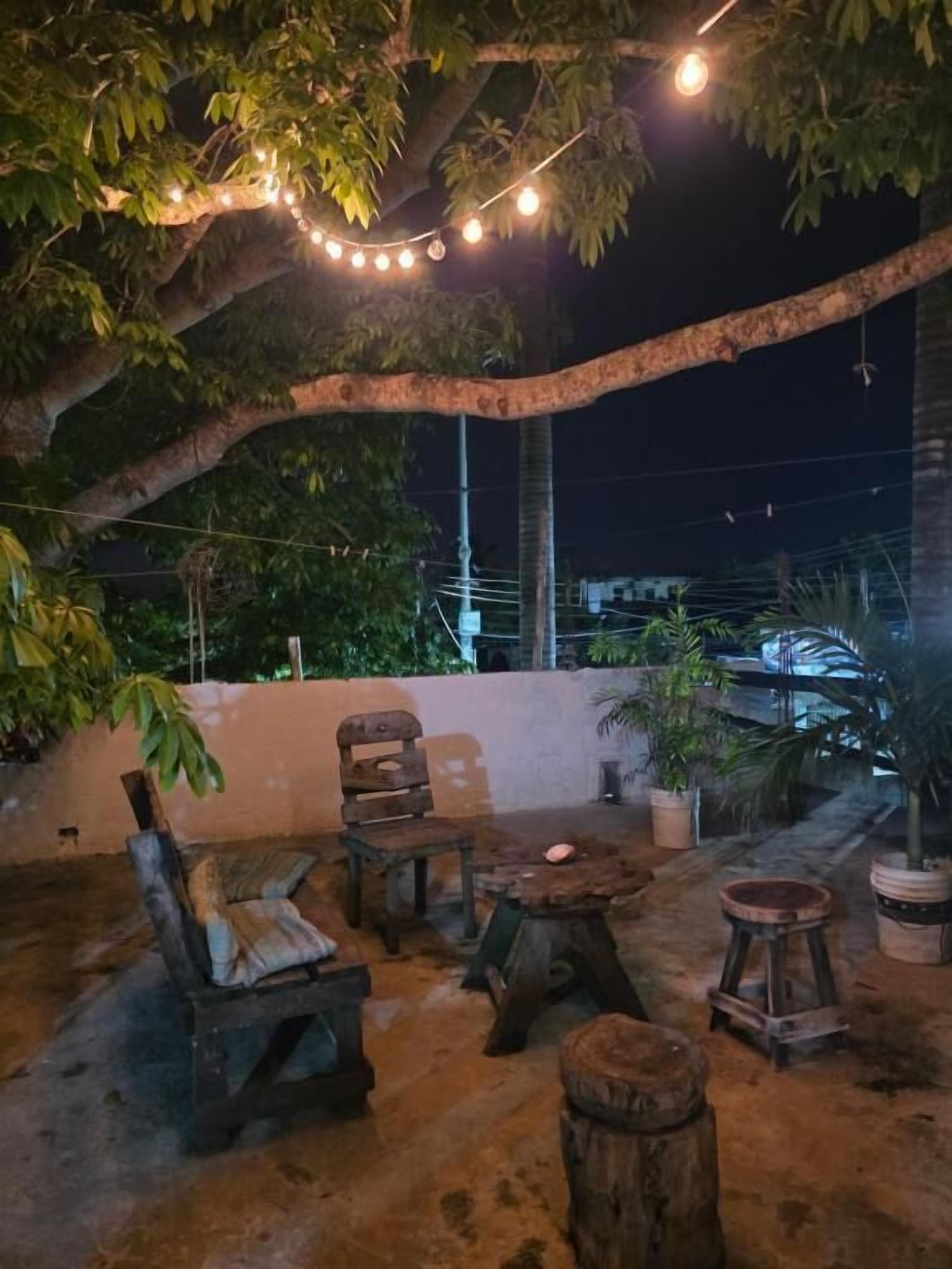 Un área de estar al aire libre con mobiliario rústico, luces colgantes y plantas en macetas.