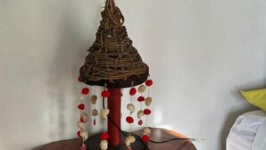 A wooden table with a decorative item on top, a white wall, and a white bed in the background. - Hostal & Camping El Árbol de la Vida. (Bacalar)